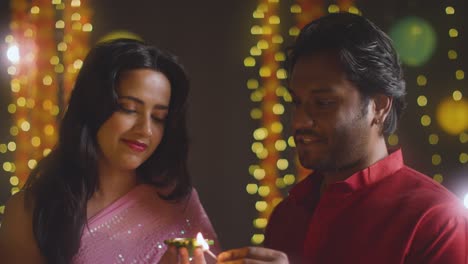 Portrait-Of-Young-Couple-Celebrating-Festival-Of-Diwali-Lighting-Diya-Oil-Lamp